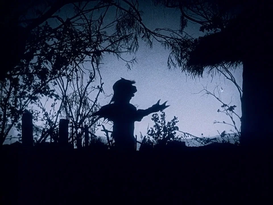 Häxan (1922) movie still: wide — A dark silhouetted figure stands in a wooded area at night. The creature extends its arms outward toward a pale…