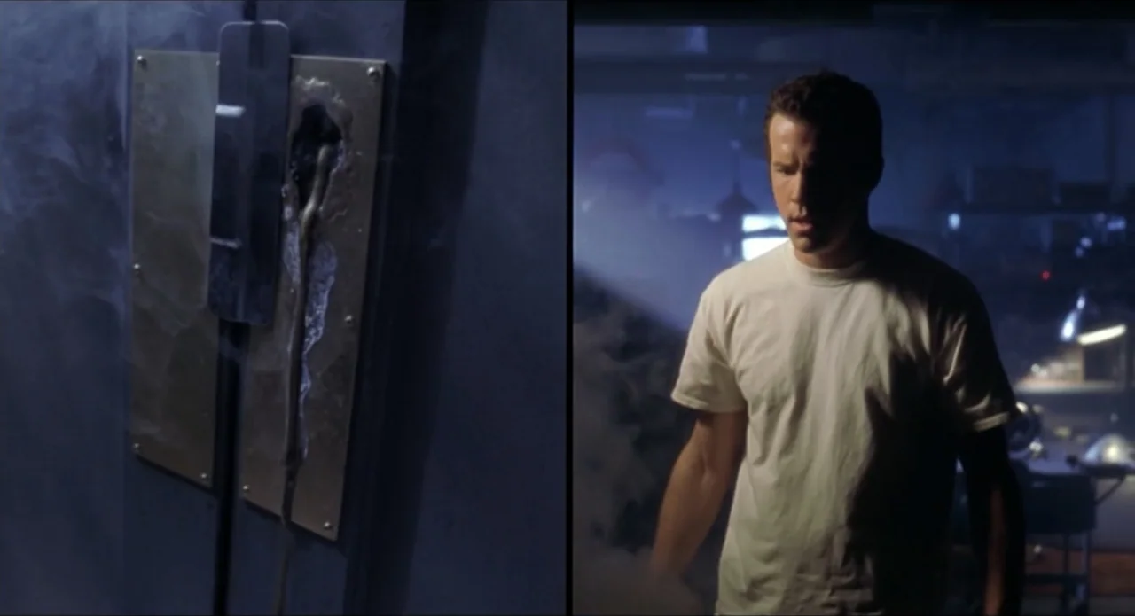 Foolproof (2003) movie still: medium — A dimly lit basement features a metal door with a charred hole in the center. A man in a white t-shirt…