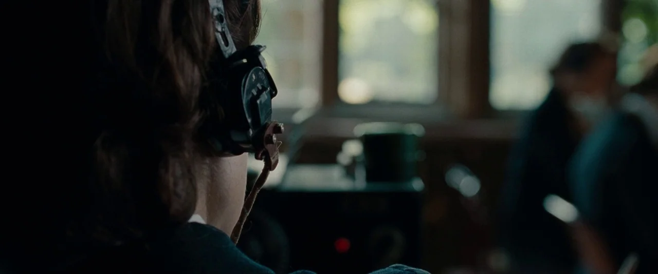 The Imitation Game (2014) movie still: closeup — A dimly lit room with vintage radio equipment and a window in the background. A woman sits wearing…