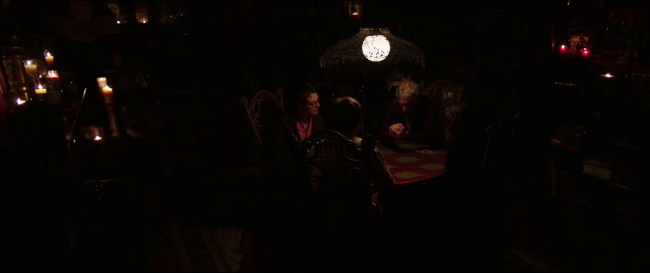 Insidious: Chapter 2 (2013) movie still: wide — Four people sit around a circular table in a dark room illuminated by candlelight. A large ornate…