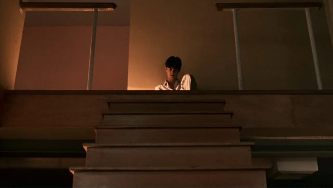 Ghost (1990) movie still: medium — A dimly lit interior with wooden stairs leading up to a small landing. A young man sits on the floor at the top…