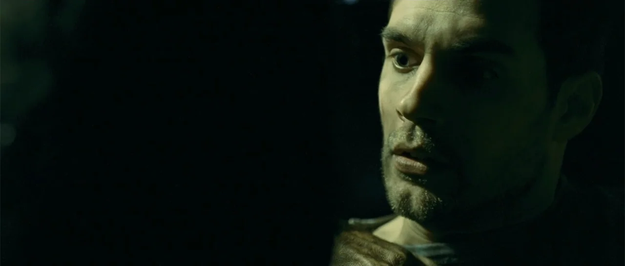 Blood Creek (2009) movie still: closeup — A dark, dimly lit interior space surrounds a man seen in close proximity. The man turns his head slightly…
