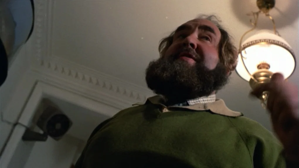 The Wicker Man movie still: medium — An interior space features white walls with decorative molding and an illuminated pendant fixture. A bearded…