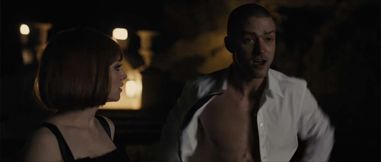 In Time (2011) movie still: medium — An outdoor night setting features a man in an unbuttoned shirt and a woman. The man speaks while looking at the…