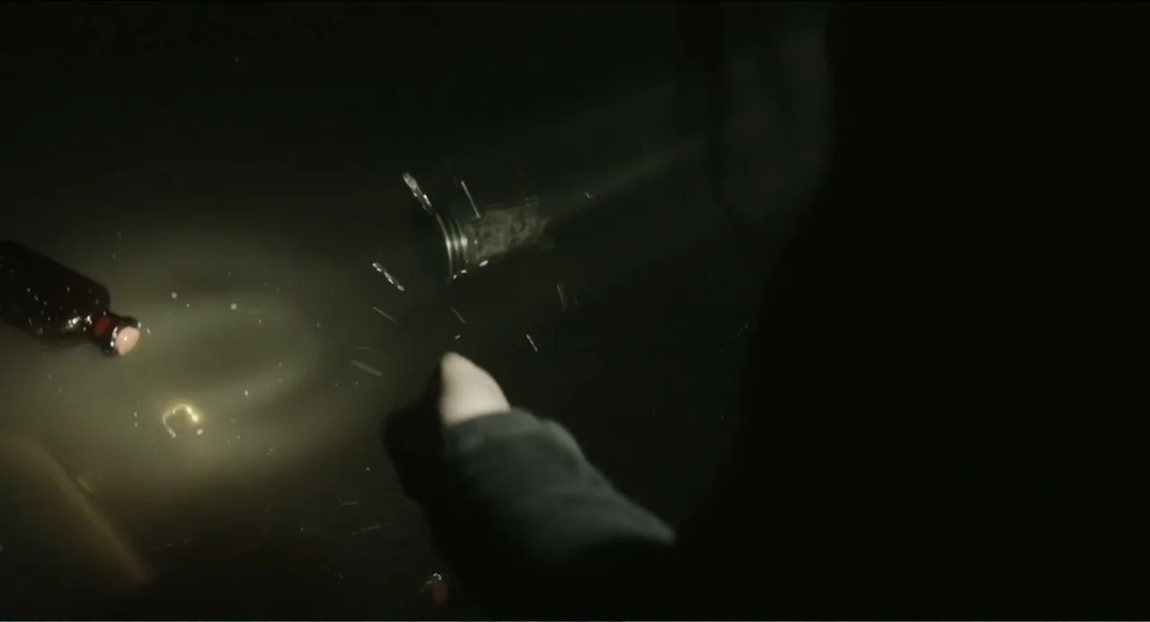 Haunter (2013) movie still: closeup — A dark, indistinguishable space is illuminated by a small, concentrated beam of light. A glass bottle rests on…