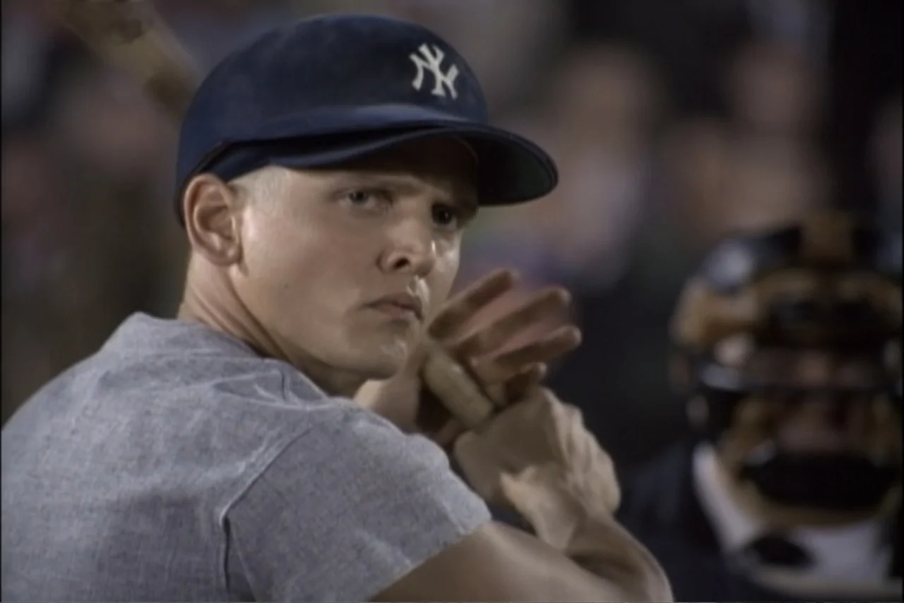 Unification of Japan 61 (2024) movie still: closeup — A baseball player in a New York Yankees cap stands in a dark field. The athlete holds a wooden…