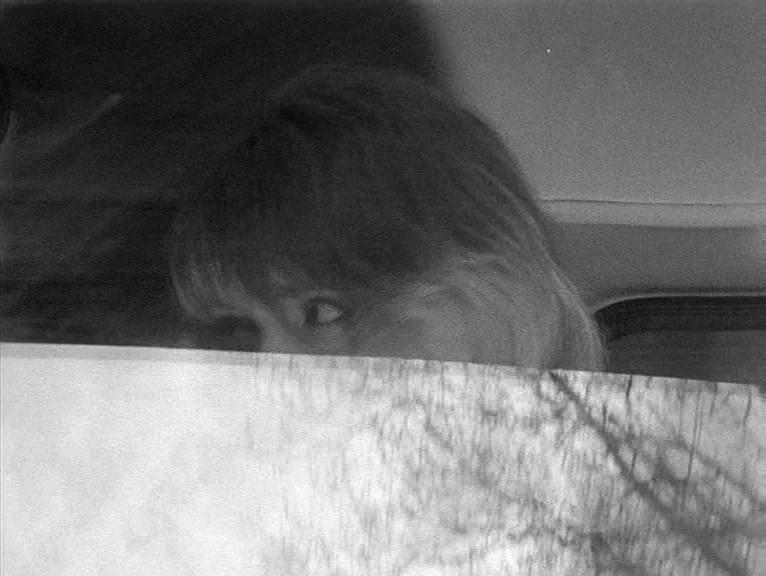 Cathy Come Home (1969) movie still: closeup — The interior of a vehicle features a person partially obscured by a printed page. The person peers…