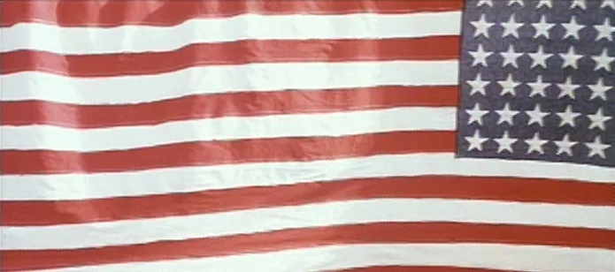 The Neon Bible (1995) movie still: closeup — A close view of an American flag with horizontal stripes and a blue canton. The fabric ripples slightly…