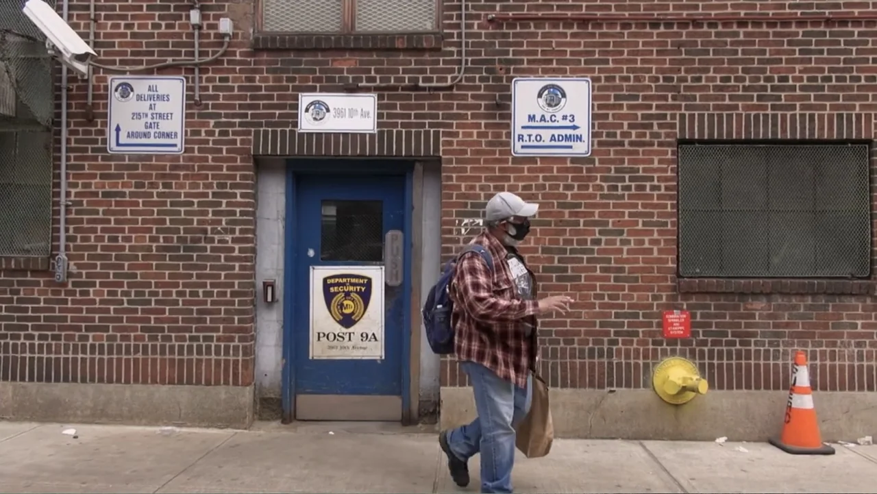 Covid Diaries NYC (2021) movie still: fullbody — A brick building exterior features a blue door labeled department of security. A man walks past the…
