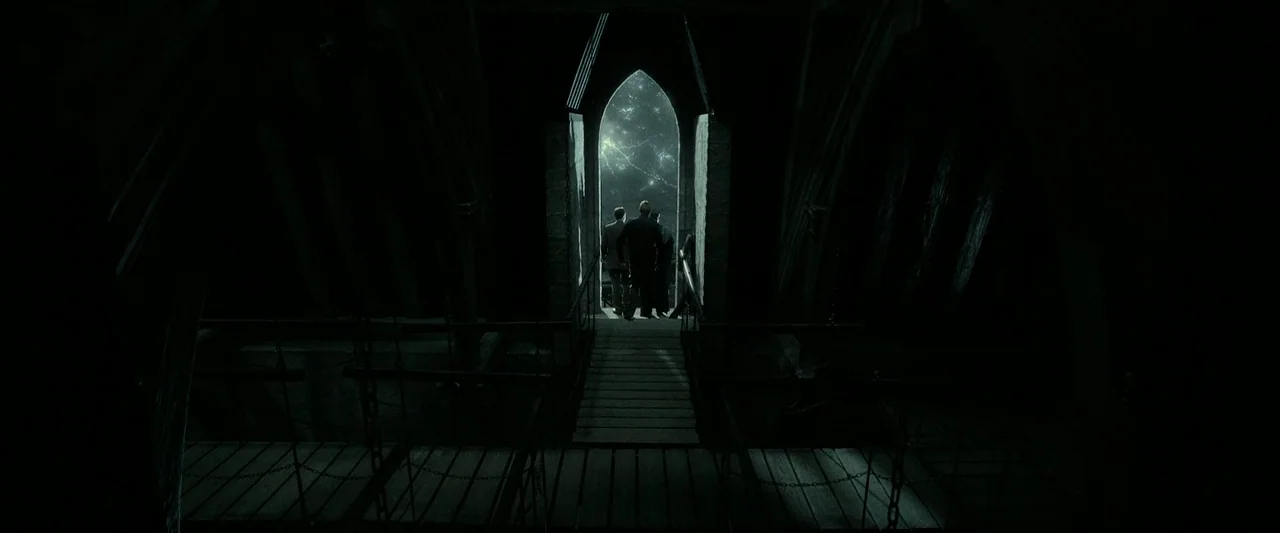 Harry Potter & The Deathly Hallows Part 2 (2011) movie still: wide — A stone tower interior with a wooden bridge leading to a high arch. Three…