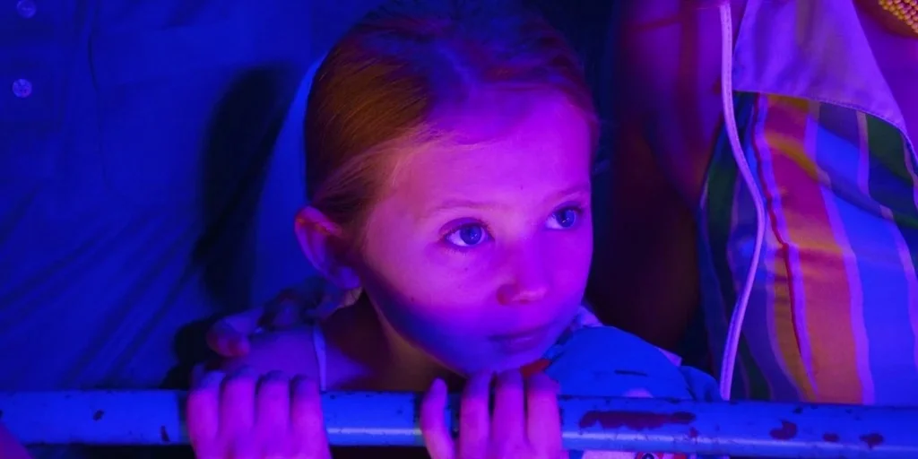 Stranger Things (2019) movie still: closeup — A dimly lit interior bathed in blue and purple light with a metal railing in the foreground. A young…