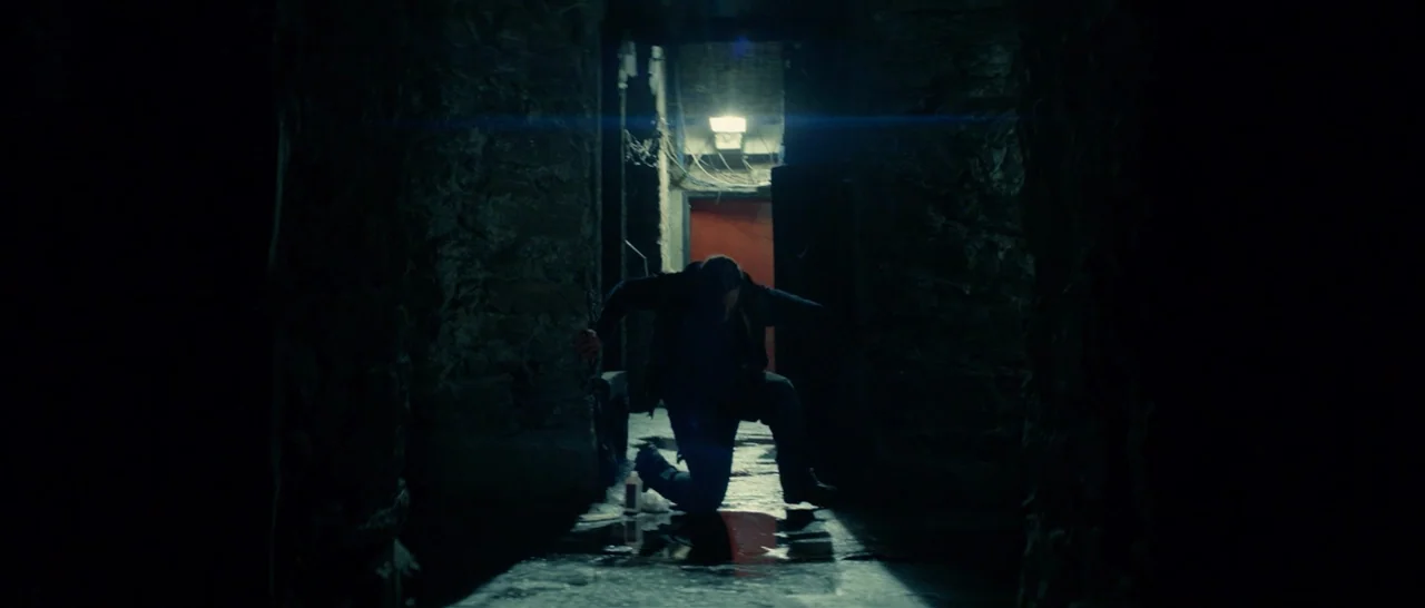 You Were Never Really Here (2017) movie still: fullbody — A narrow dark tunnel with rough stone walls features a wet, reflective floor. A lone man…