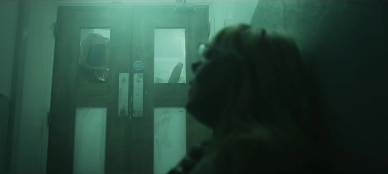 Containment (2015) movie still: medium — A dimly lit hospital corridor features a wooden double door with frosted glass panels. A person stands in…