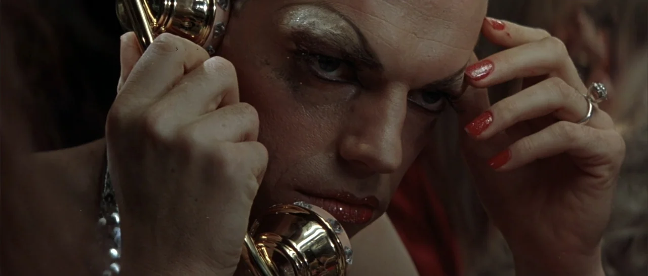 The Adventures of Priscilla, Queen of the Desert (1994) movie still: closeup — A dimly lit interior space focusing on a person in heavy makeup and…