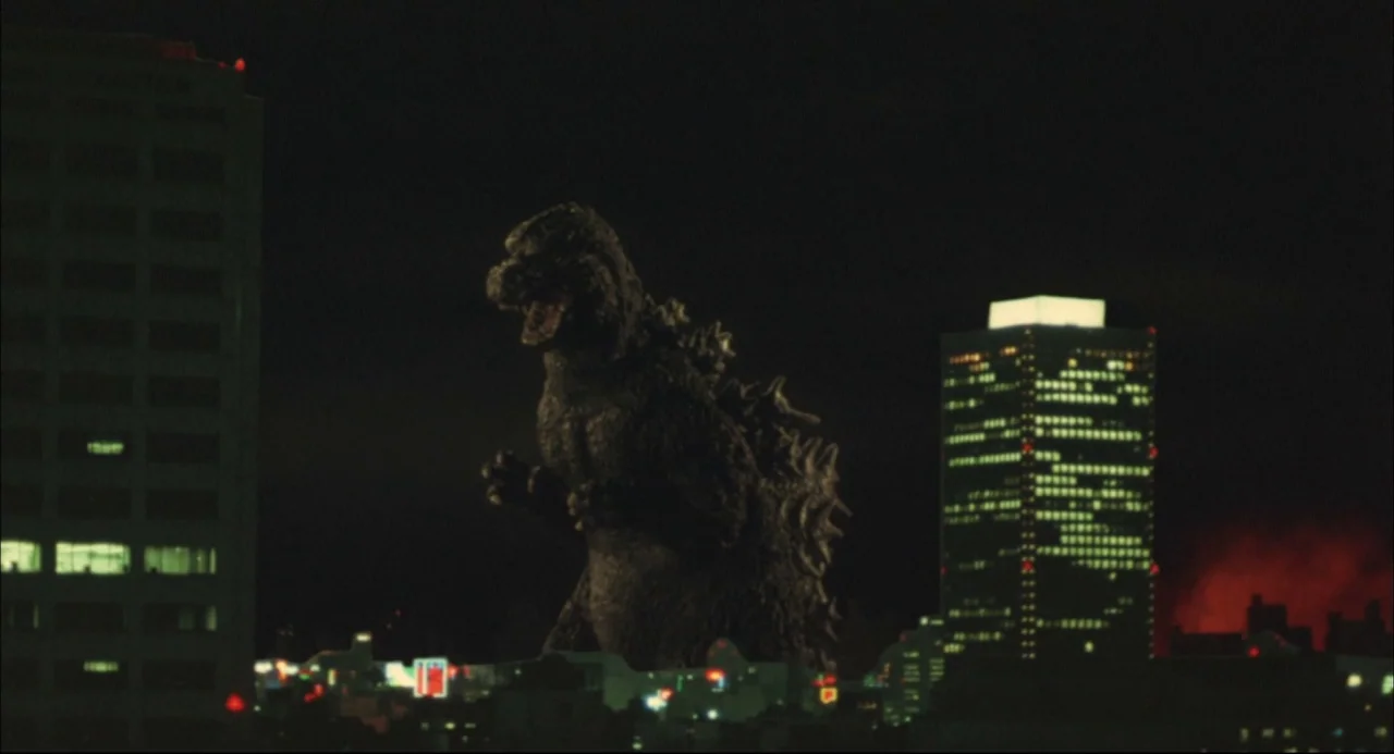 The Return of Godzilla (1984) movie still: wide — A dark city skyline at night features a towering monster in the center foreground. A large office…