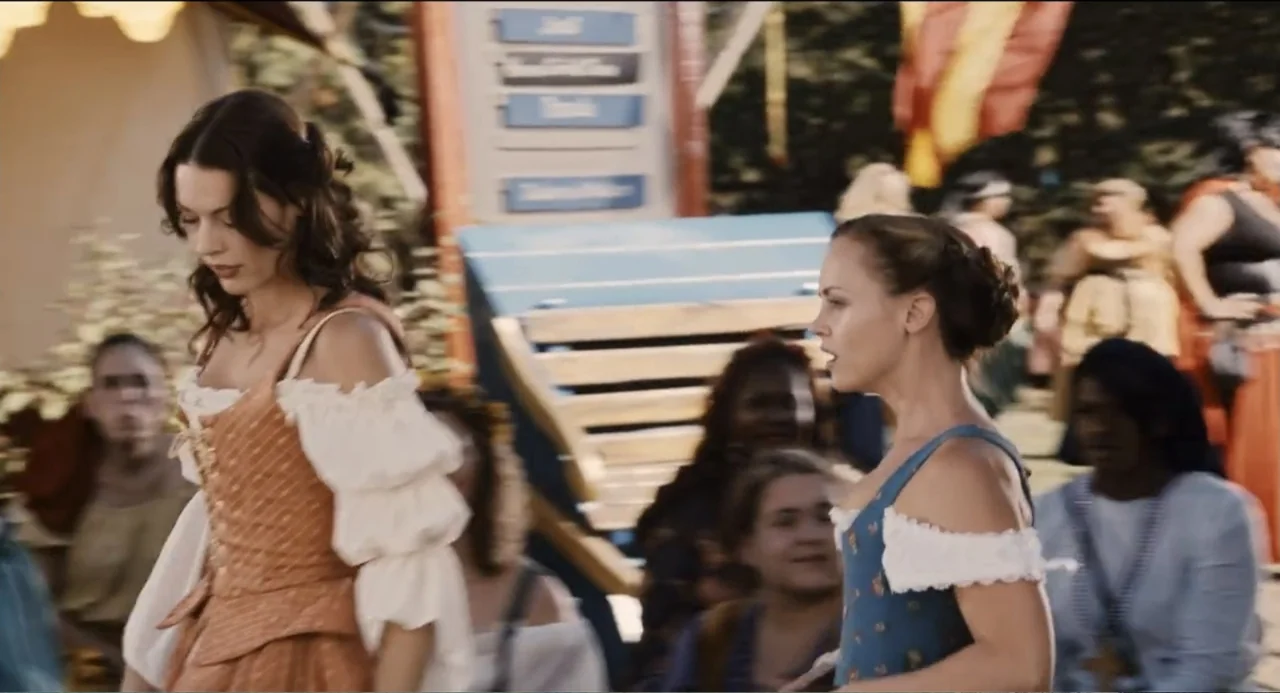 Todo es amor (2024) movie still: medium — An outdoor fair with colorful booths and a crowd of people in costumes. Two women in period-appropriate…