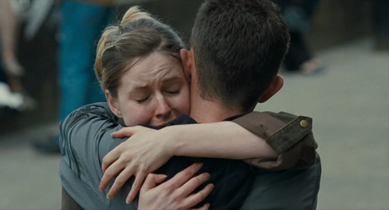 The Angel’s Share (2012) movie still: medium — A couple embraces in a public space with other people blurred in the background. A woman holds onto a…