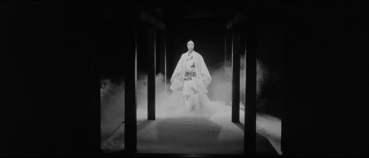 Kuroneko (1968) movie still: fullbody — A dark, dimly lit corridor features vertical wooden supports on either side. A woman in a white kimono…