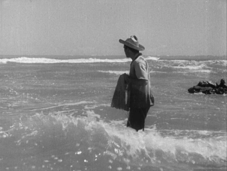 Redes (1936) movie still: fullbody — A man stands knee-deep in ocean surf during the daylight. He holds a fishing net while looking toward the…