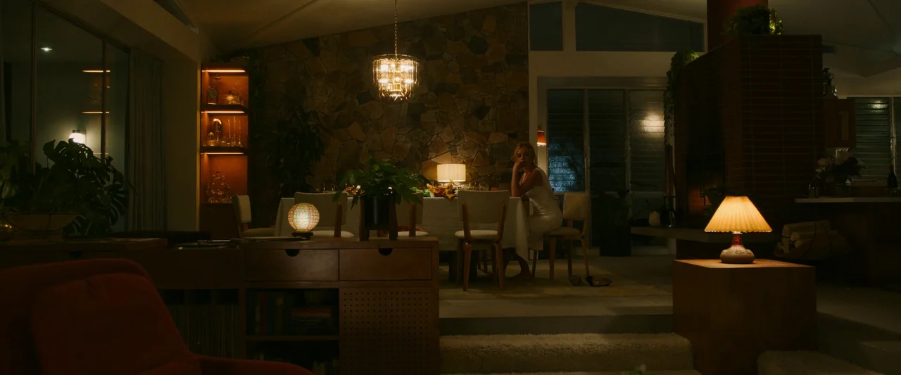 Don’t Worry Darling (2022) movie still: wide — A mid-century modern open-concept space features a stone wall and split-level floor plan. A woman in…