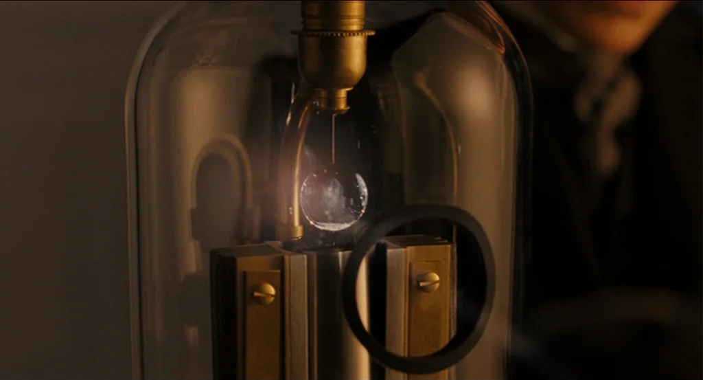 A Dangerous Method movie still: closeup — A glass vacuum tube contains a small metallic apparatus with a centered glowing orb. The device features…