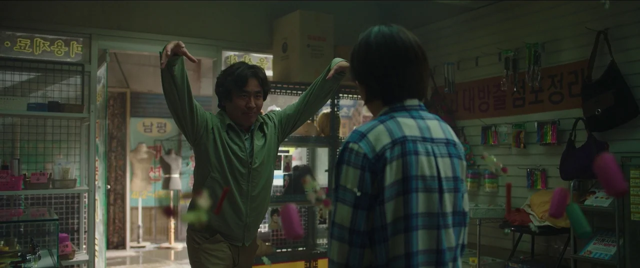 Psychokinesis (2018) movie still: medium — A cluttered retail space contains shelves filled with colorful hair rollers and miscellaneous products. A…