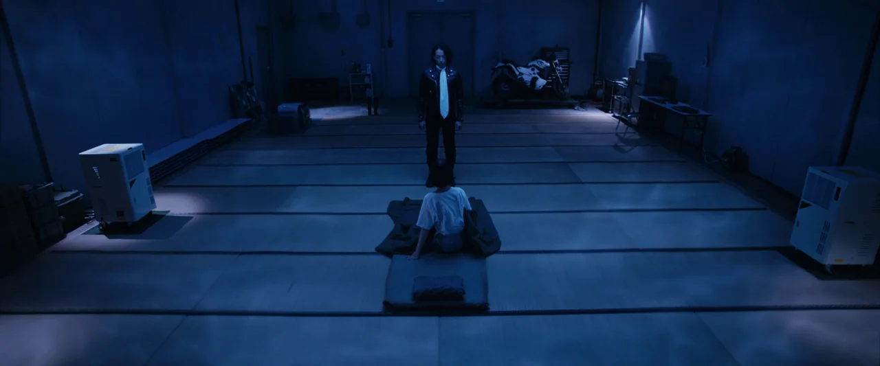 Shin Kamen Rider (2023) movie still: wide — A dark, expansive industrial space features a tatami-matted floor with industrial equipment visible. A…