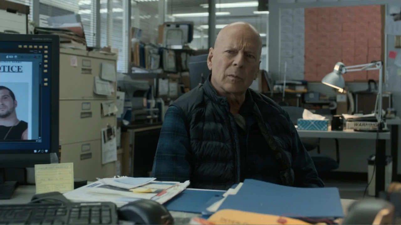 Death Wish (2018) movie still: medium — A cluttered police office contains metal filing cabinets and monitors displaying digital documents. An older…