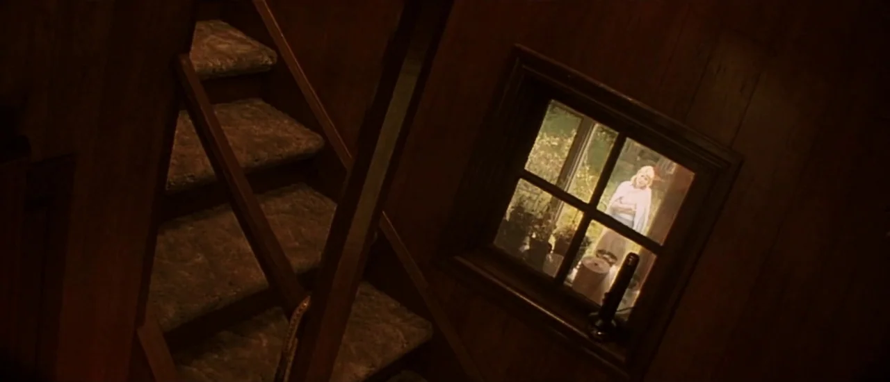 Dancer in the Dark (2000) movie still: wide — A dark, wood-paneled stairwell features a small window looking out to a sunny exterior. A woman stands…