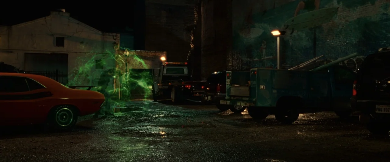 Green Lantern (2011) movie still: wide — A dark, damp concrete parking lot is filled with parked trucks and cars at night. A luminous green portal…