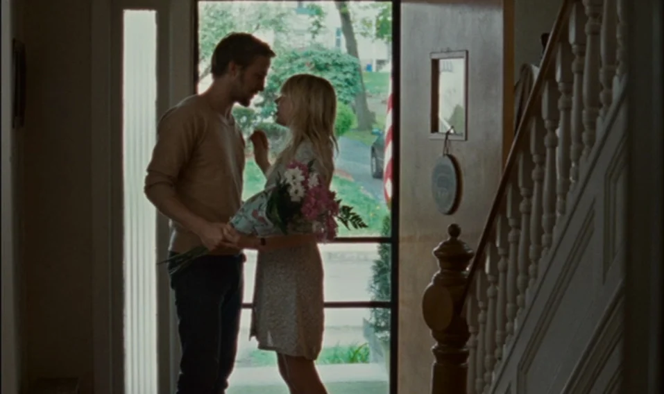 Blue Valentine (2010) movie still: medium — A residential entryway with a wooden staircase and an open front door. A man and a woman stand together…