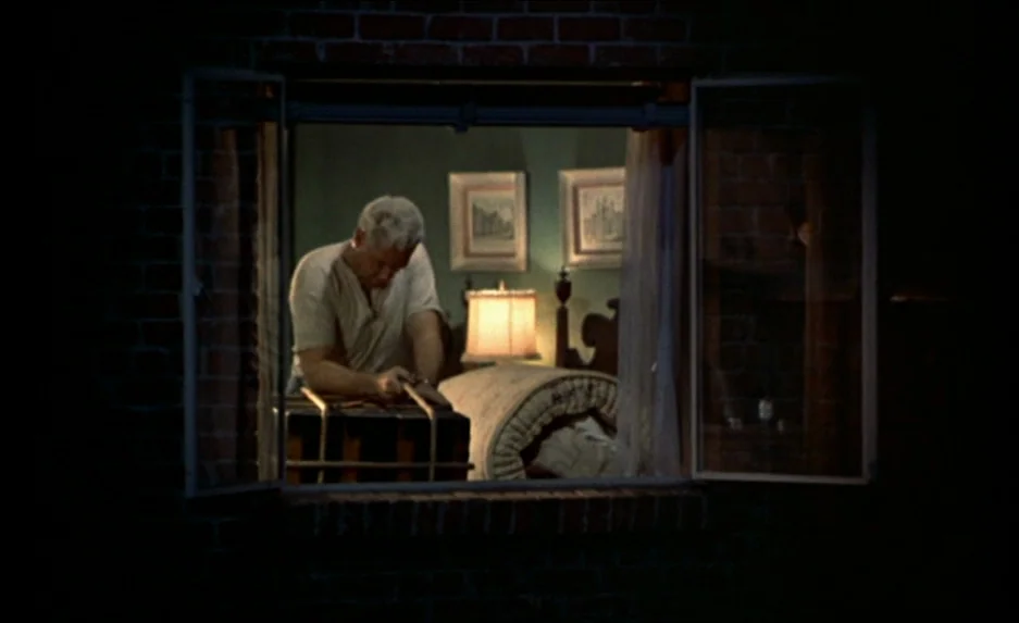 Rear Window (1954) movie still: medium — A brick-framed open window looks into a dimly lit room with green walls. An older man leans his arms on a…