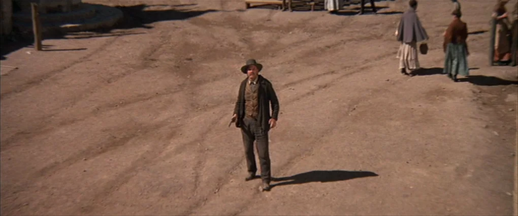 Pat Garrett & Billy The Kid (1973) movie still: fullbody — A dusty, sun-baked plaza features dry earth marked with wagon wheel tracks and…