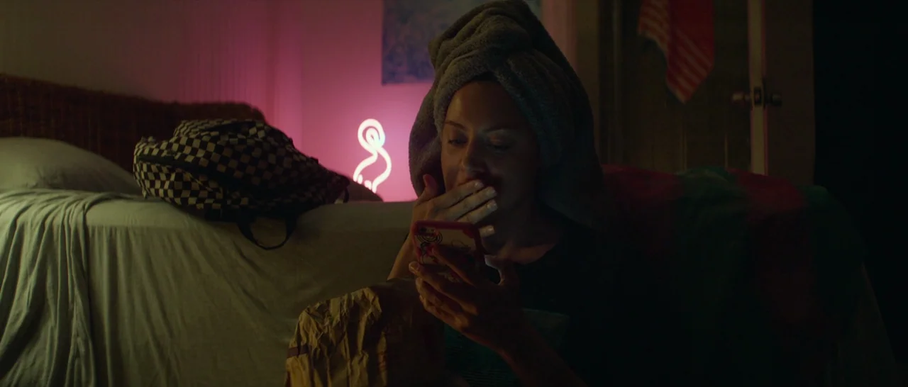 Ingrid Goes West (2017) movie still: medium — A dimly lit room features a bed with a checkered backpack on top. A woman with a towel on her head…
