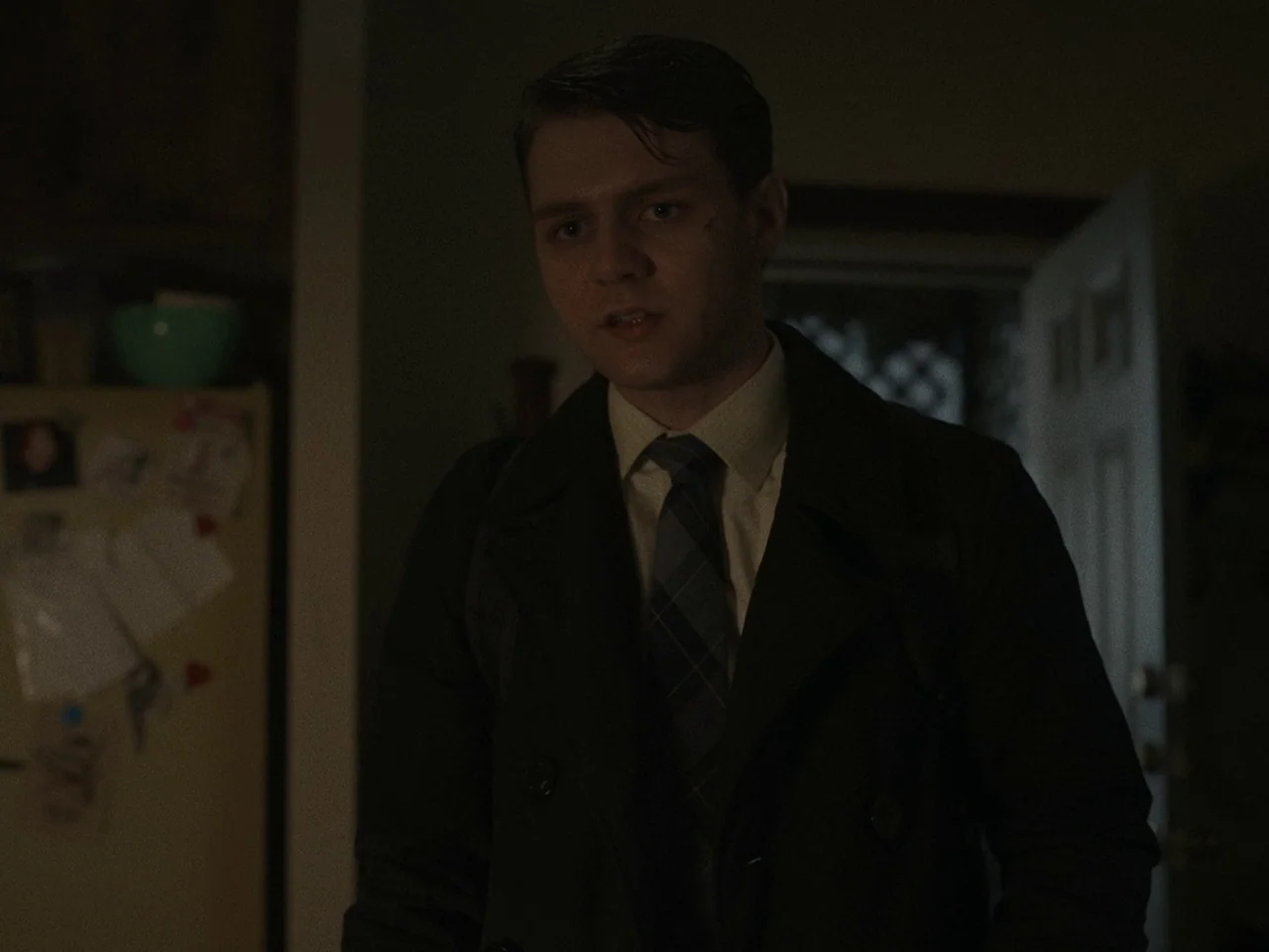 The Whale (2022) movie still: medium — A dimly lit room with a refrigerator covered in notes in the background. A young man wearing a coat and tie…