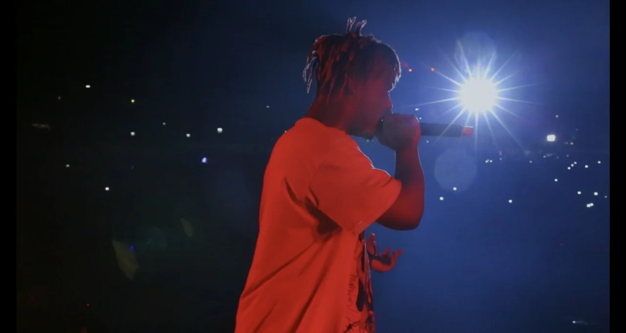 Juice WRLD: Into the Abyss (2021) movie still: medium — A dark, expansive concert arena with blurred audience lights in the background. A young male…