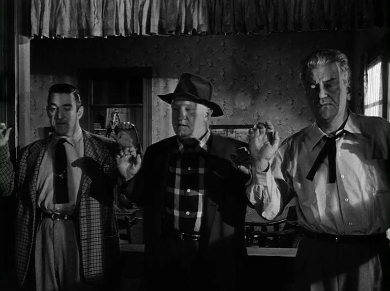 The Killing (1956) movie still: medium — A dark living room with floral wallpaper and a curtained window. Three men stand together holding their…