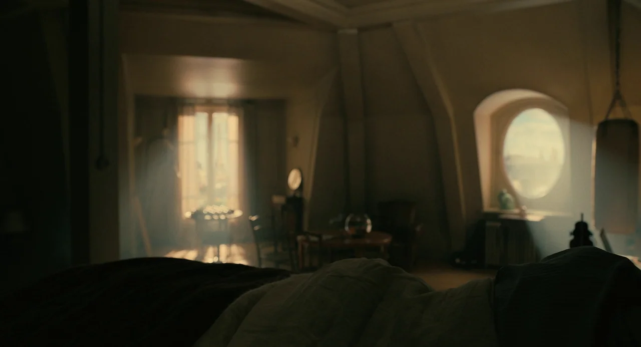 The Killer (2024) (2024) movie still: wide — A spacious room features sloped walls, a circular window, and soft morning sunlight. The foreground…