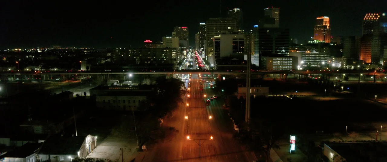 Renfield (2023) movie still: establishing — An aerial night view of a multi-lane city avenue stretching toward distant skyscrapers. A highway…