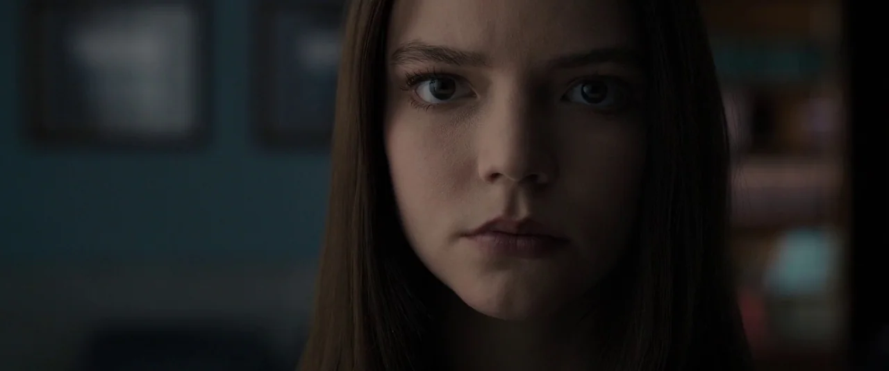 Glass (2019) movie still: closeup — A dimly lit room provides a blurred background for a close portrait. A young woman looks forward with a neutral…