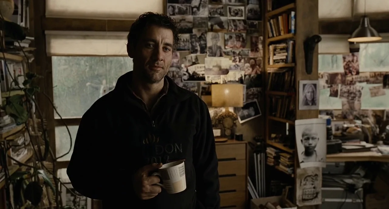 Children Of Men (2006) movie still: medium — A cluttered room contains shelves filled with books and walls covered in taped photographs. A man in a…