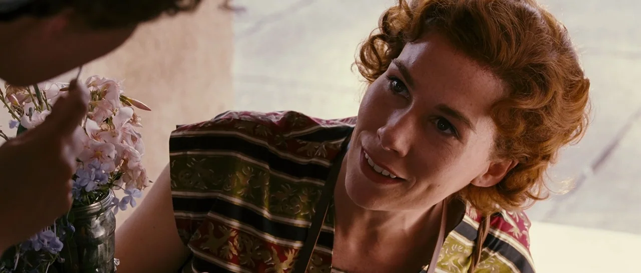 Black Book (2006) movie still: medium — A sunlit retail space features shelves and a glass jar filled with small wildflowers. A woman with wavy…