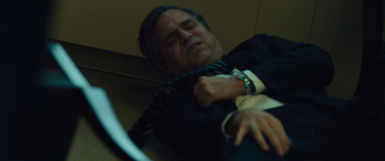 Dark Waters (2019) movie still: medium — A dimly lit room with plain walls provides the backdrop for the fallen man. A middle-aged man in a suit…
