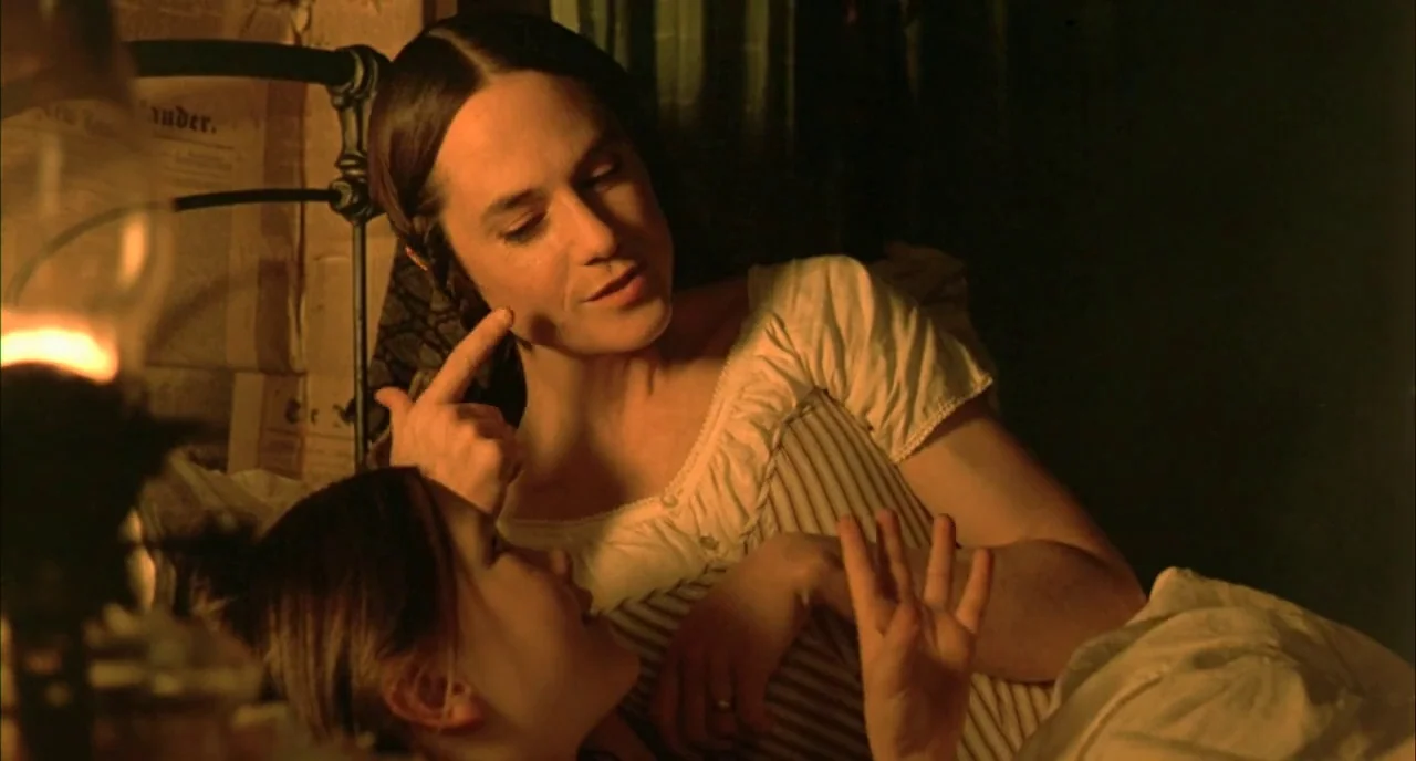 The Piano (1993) movie still: medium — A dimly lit room contains an iron bed frame and textured wall covering. One woman lies down while the other…