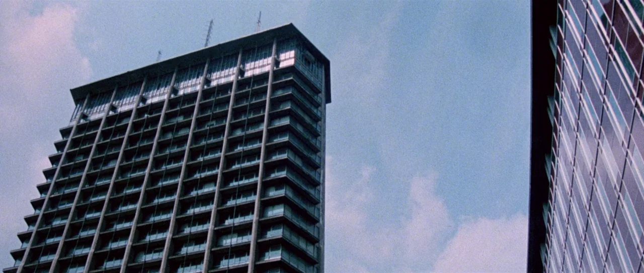 The Suspicious Death of a Minor (1975) movie still: establishing — A tall mid-century modern concrete skyscraper stands beside another glass…