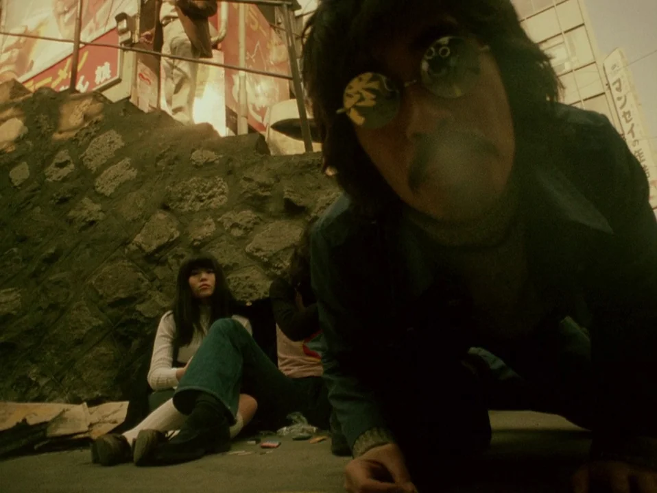 Throw Away Your Books, Rally in the Streets (1971) movie still: closeup — An urban setting with a rough stone wall and visible Japanese commercial…
