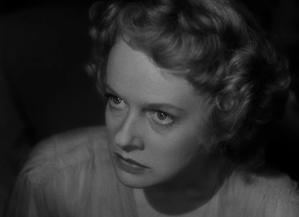 Citizen Kane (1941) movie still: closeup — An interior space is cast in darkness, focusing on a woman's face. The woman gazes intently upward while…