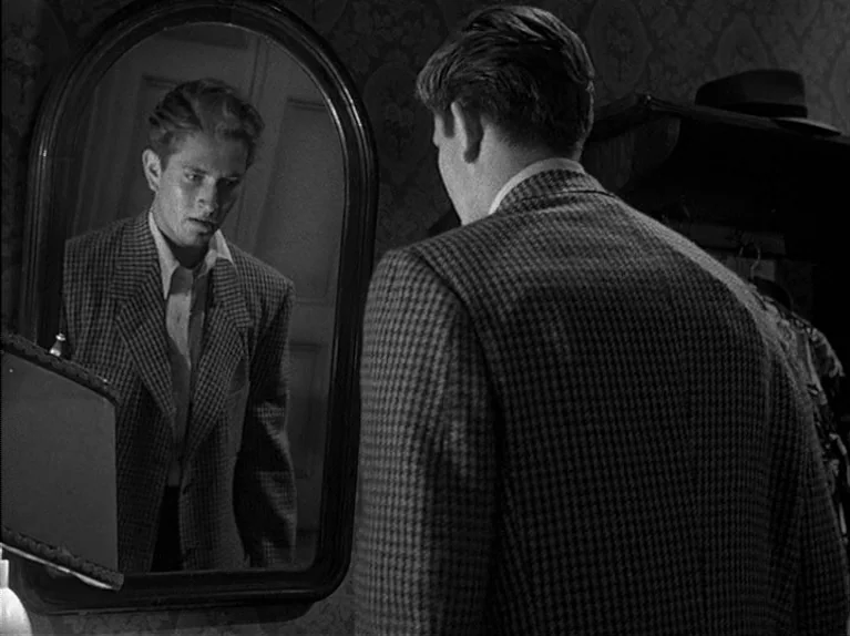 The Big Night (1951) movie still: medium — A dimly lit dressing area features floral wallpaper and a dark wooden clothes rack. A man in a…