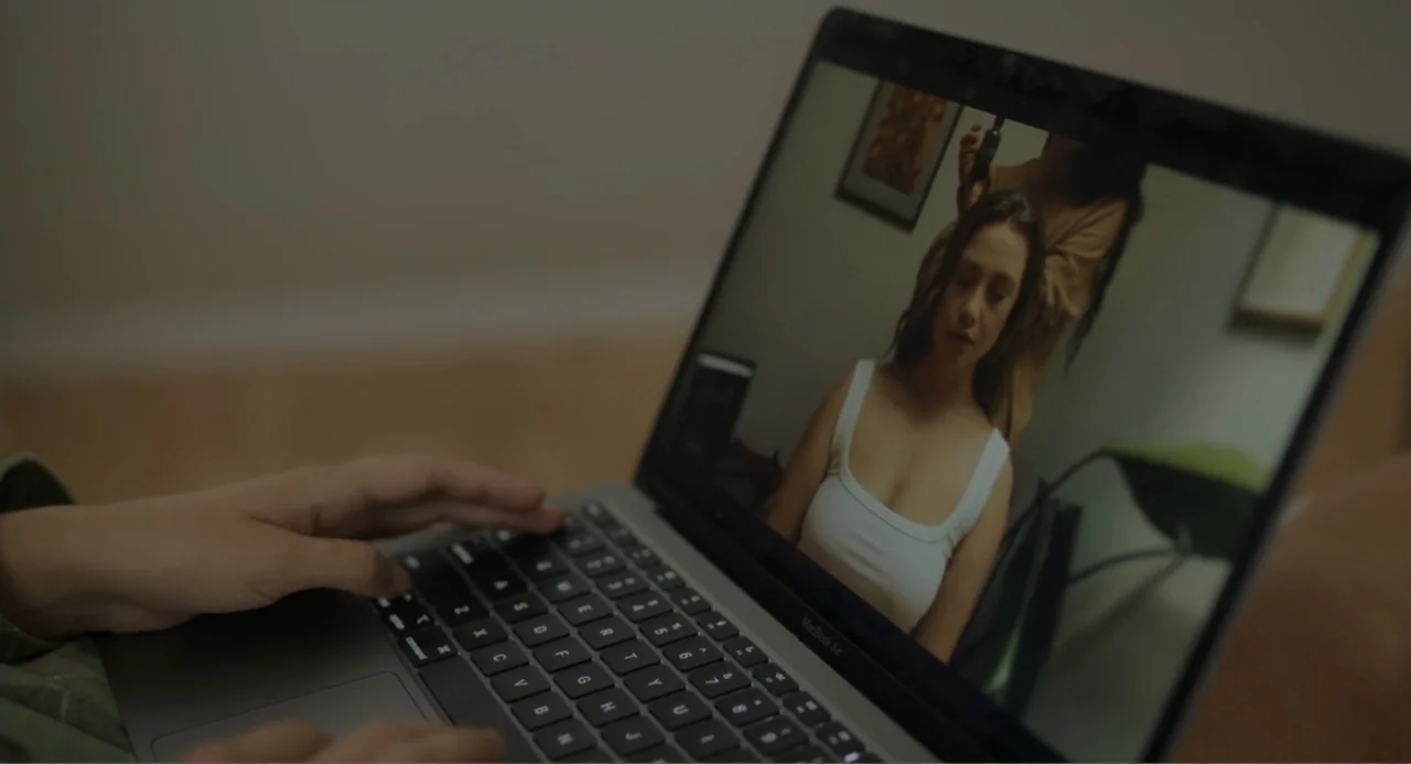 This Closeness (2024) movie still: medium — A close-up view of a person's hands operating a laptop in an interior space. The laptop screen displays…