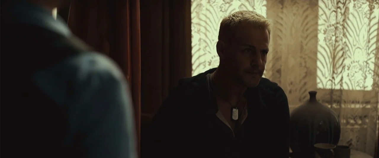The Condemned 2 (2015) movie still: medium — A dimly lit interior space features ornate patterned wallpaper and draped fabric curtains. A man with…